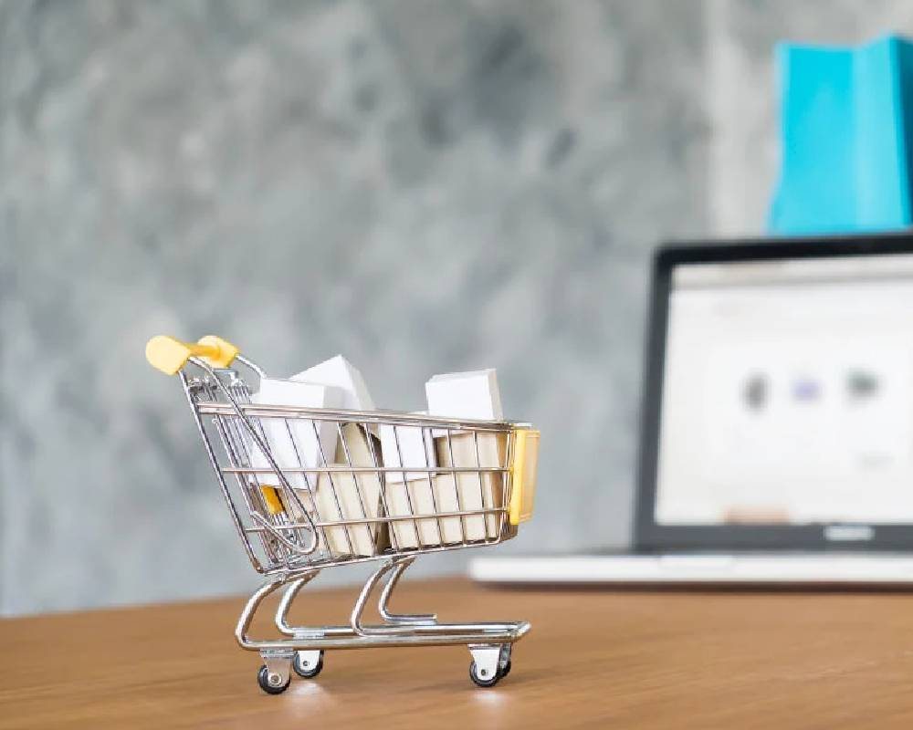 A small shopping cart filled with parcels next to a laptop